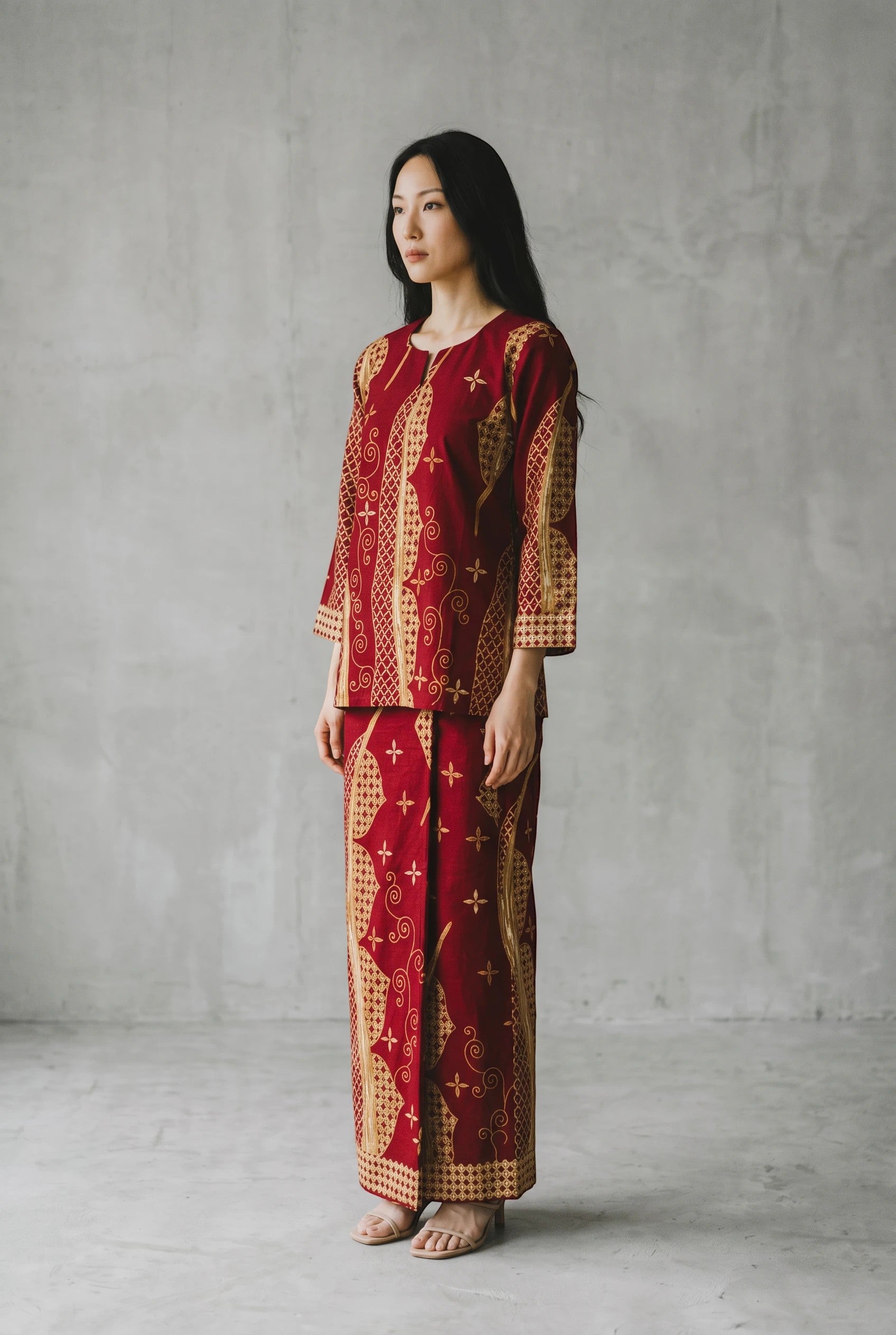 A model wearing a maroon PARCA cotton top and matching maxi sarung with traditional gold batik-inspired patterns.