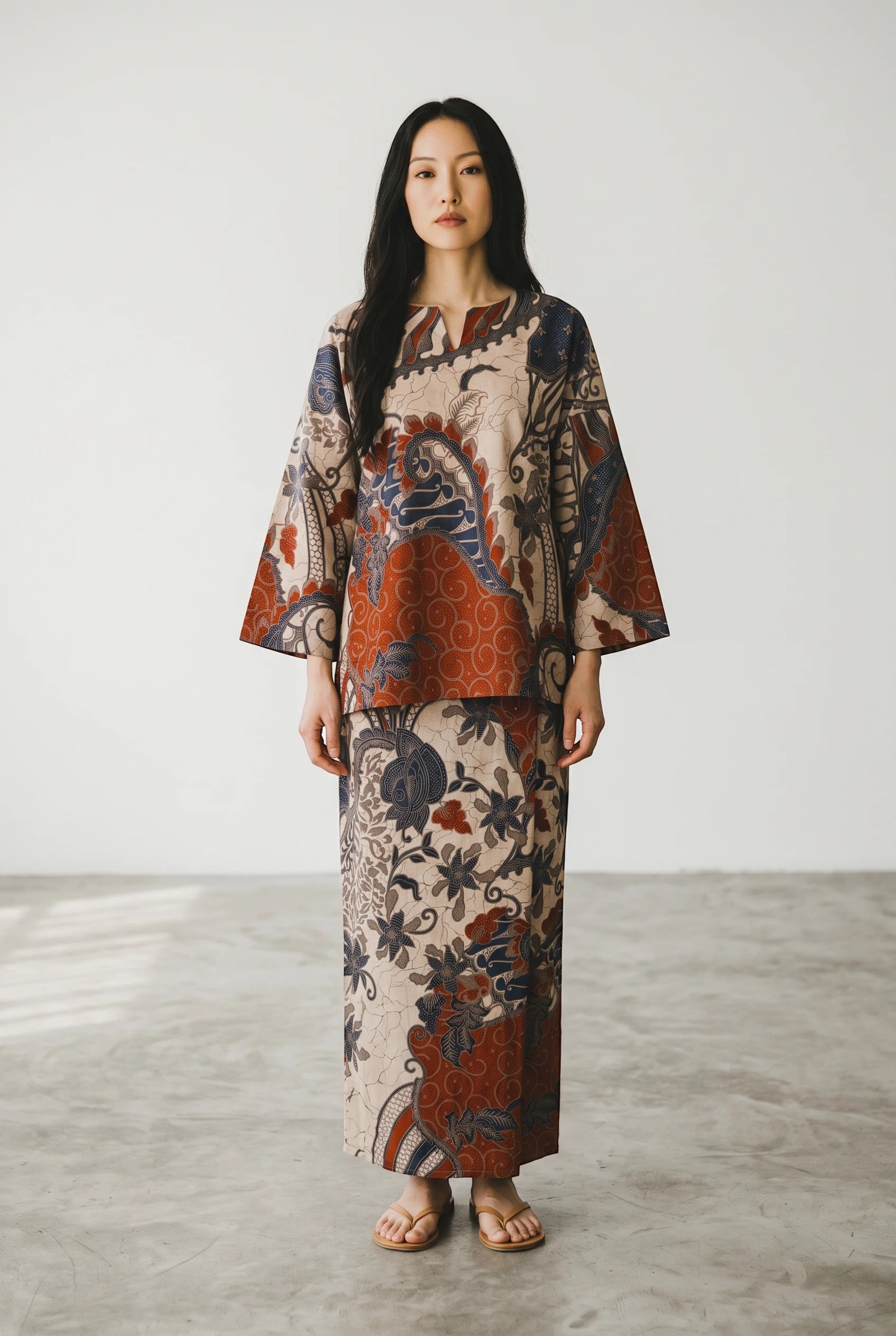 PARCA Mastura set in orange featuring traditional batik floral patterns on a long-sleeved top and matching skirt.