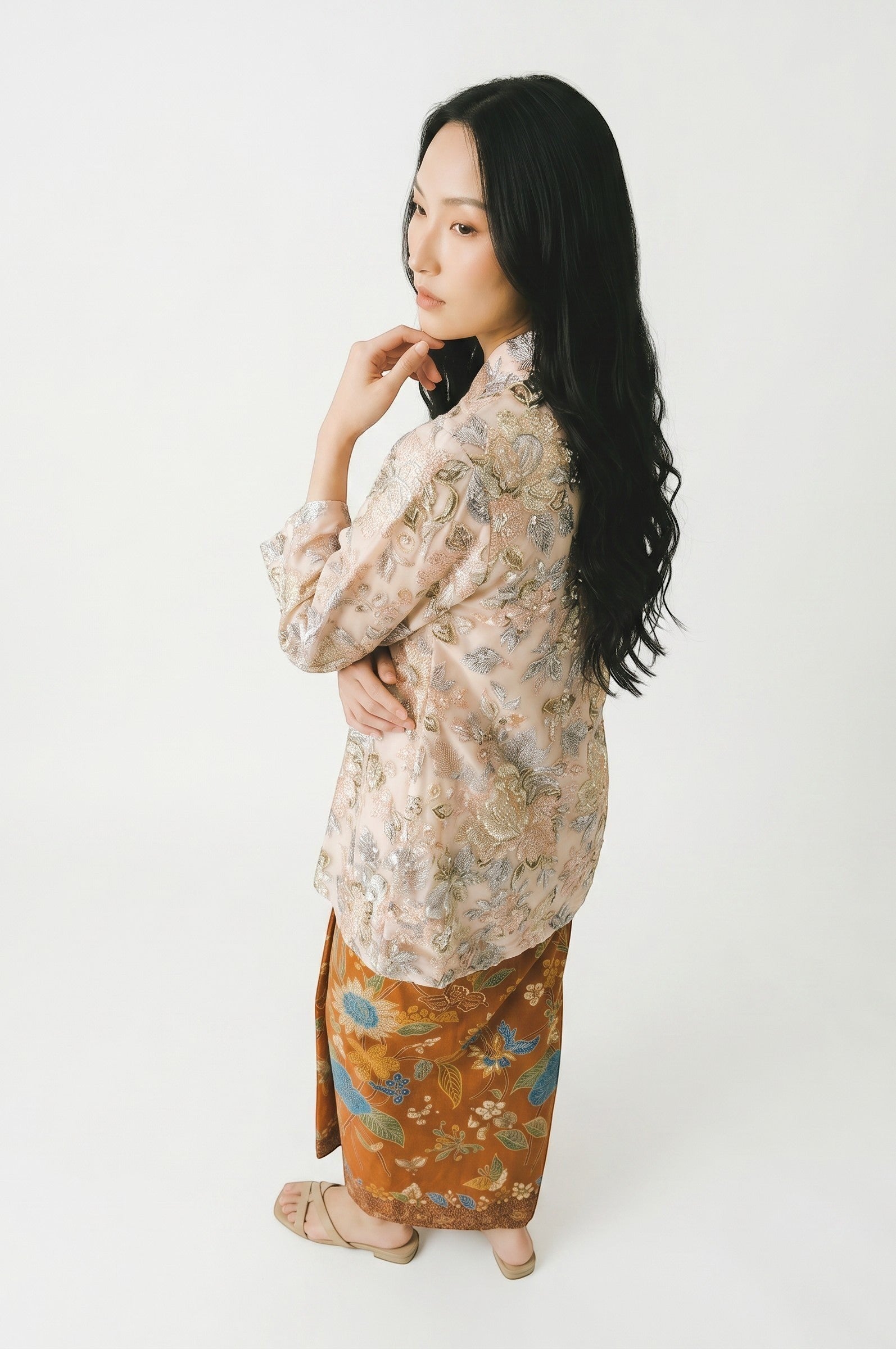 PARCA Naira Kimono kebaya in light peach with intricate floral embroidery and beading, paired with a brown batik sarong.