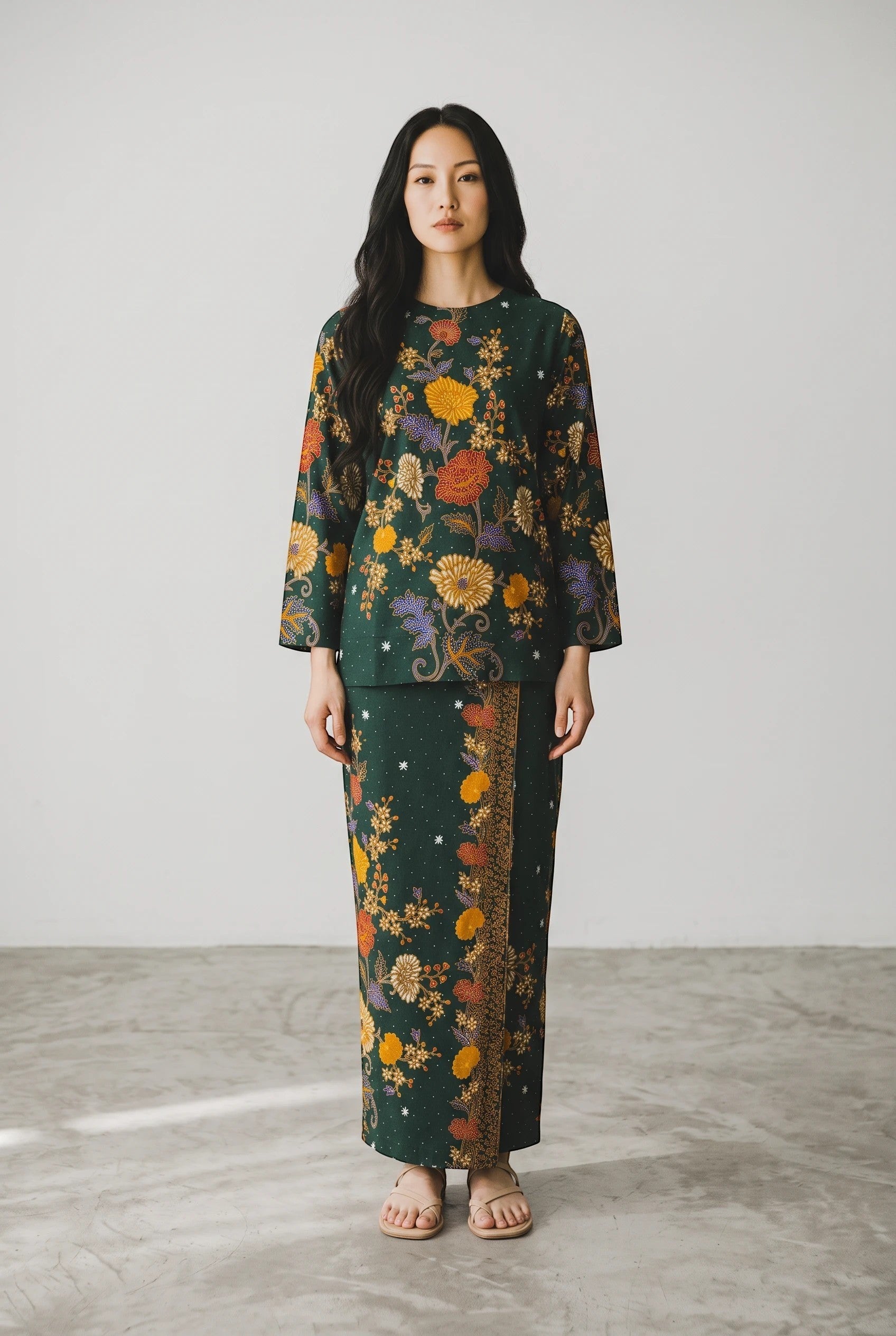 A woman wearing a PARCA Nayra green long-sleeved batik set with intricate floral patterns and a matching sarong skirt.