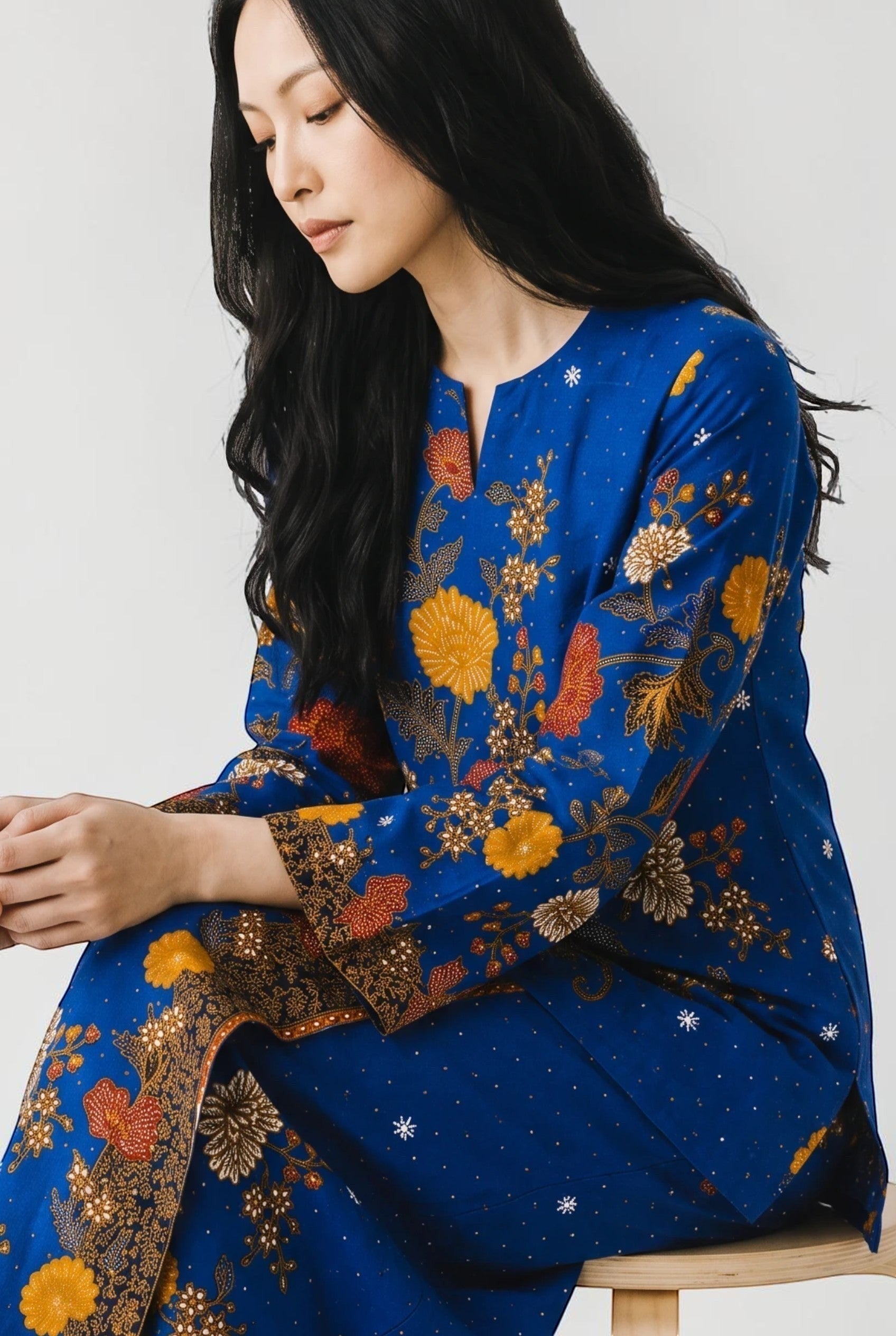 PARCA Nayra royal blue cotton top and sarung set with floral batik pattern, worn by a model sitting on a stool.