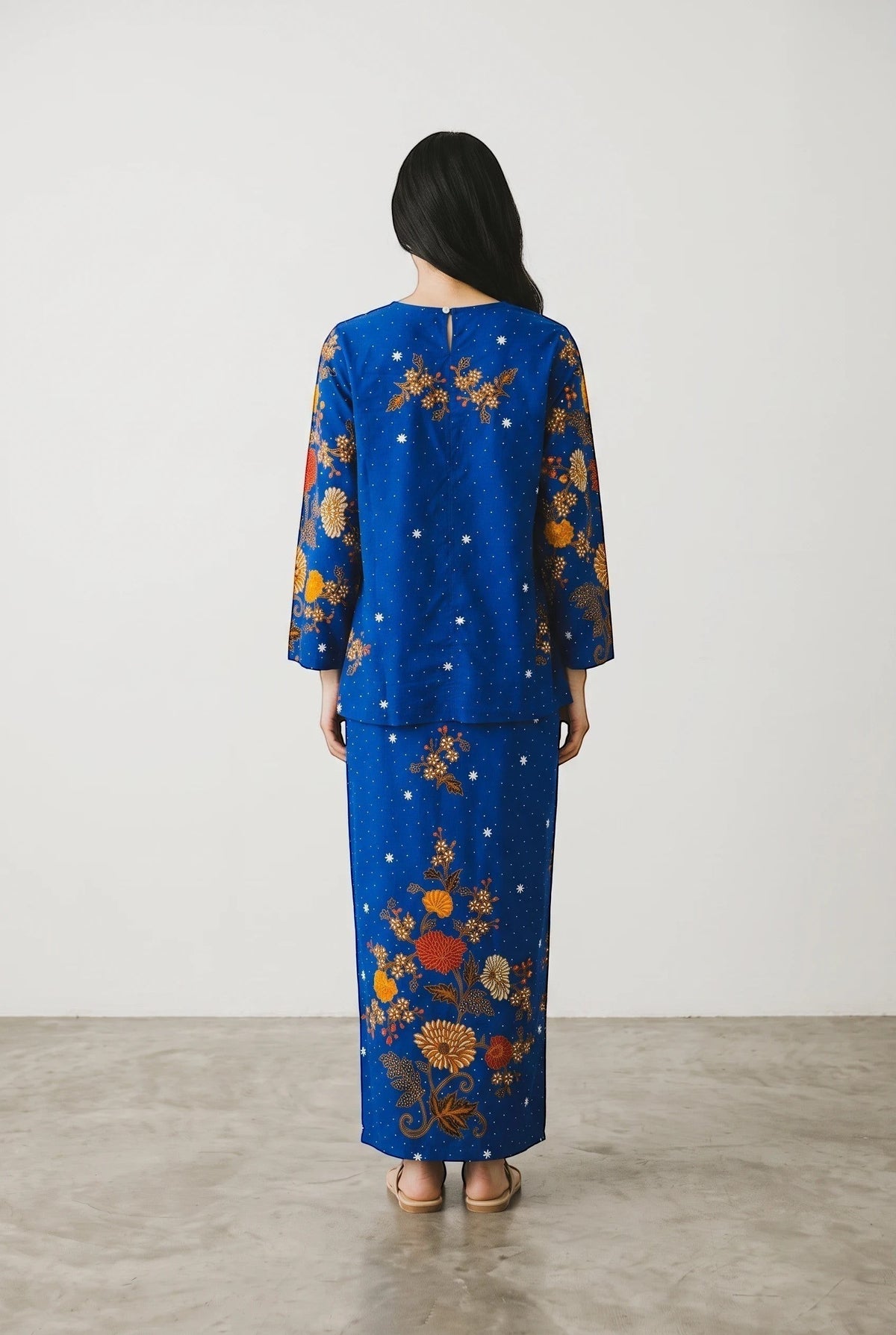 Back view of a woman wearing a PARCA royal blue cotton top and matching sarung with floral batik-style print.