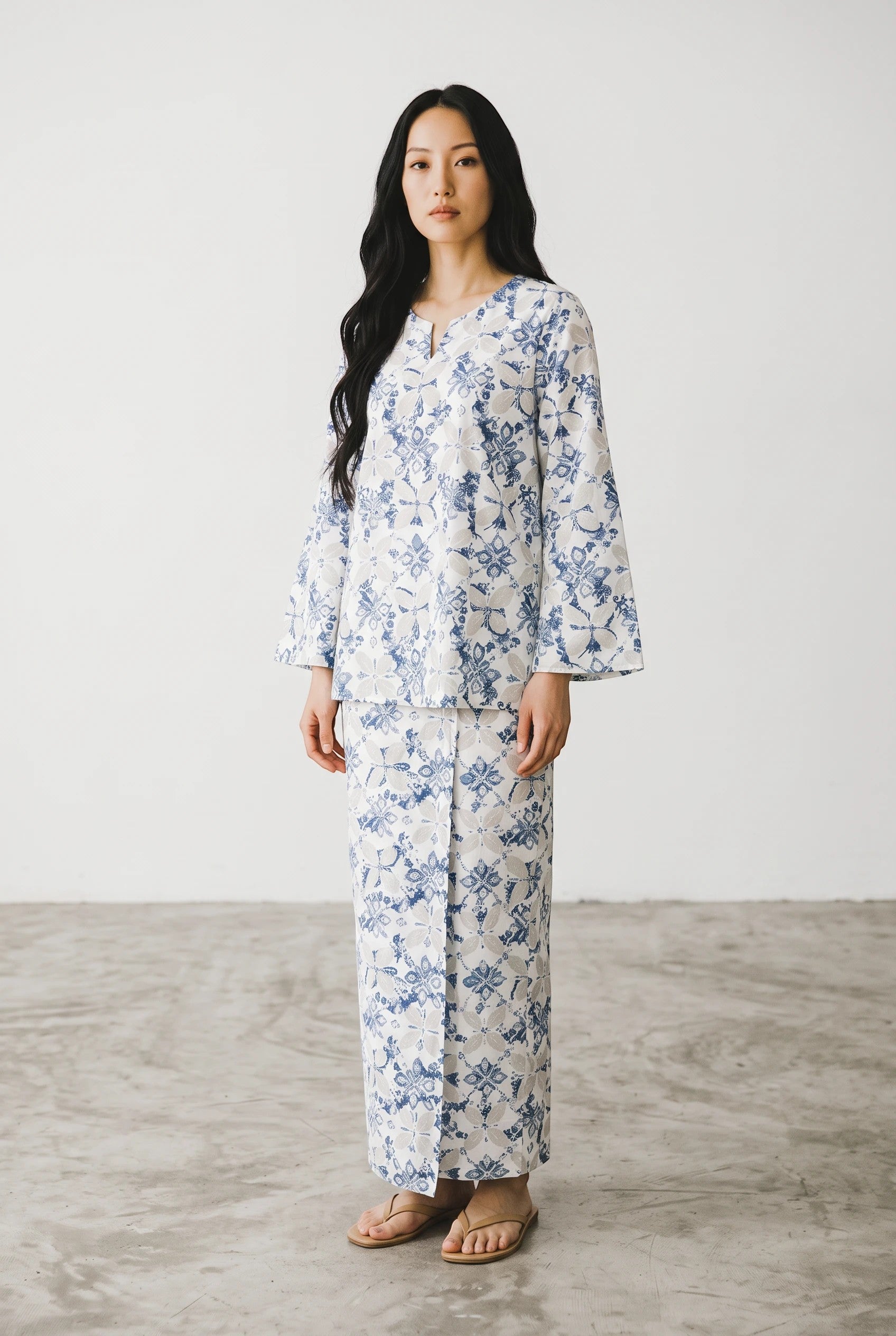 Model wearing a PARCA white midi top and matching maxi sarung with a blue floral print and relaxed oversized fit.