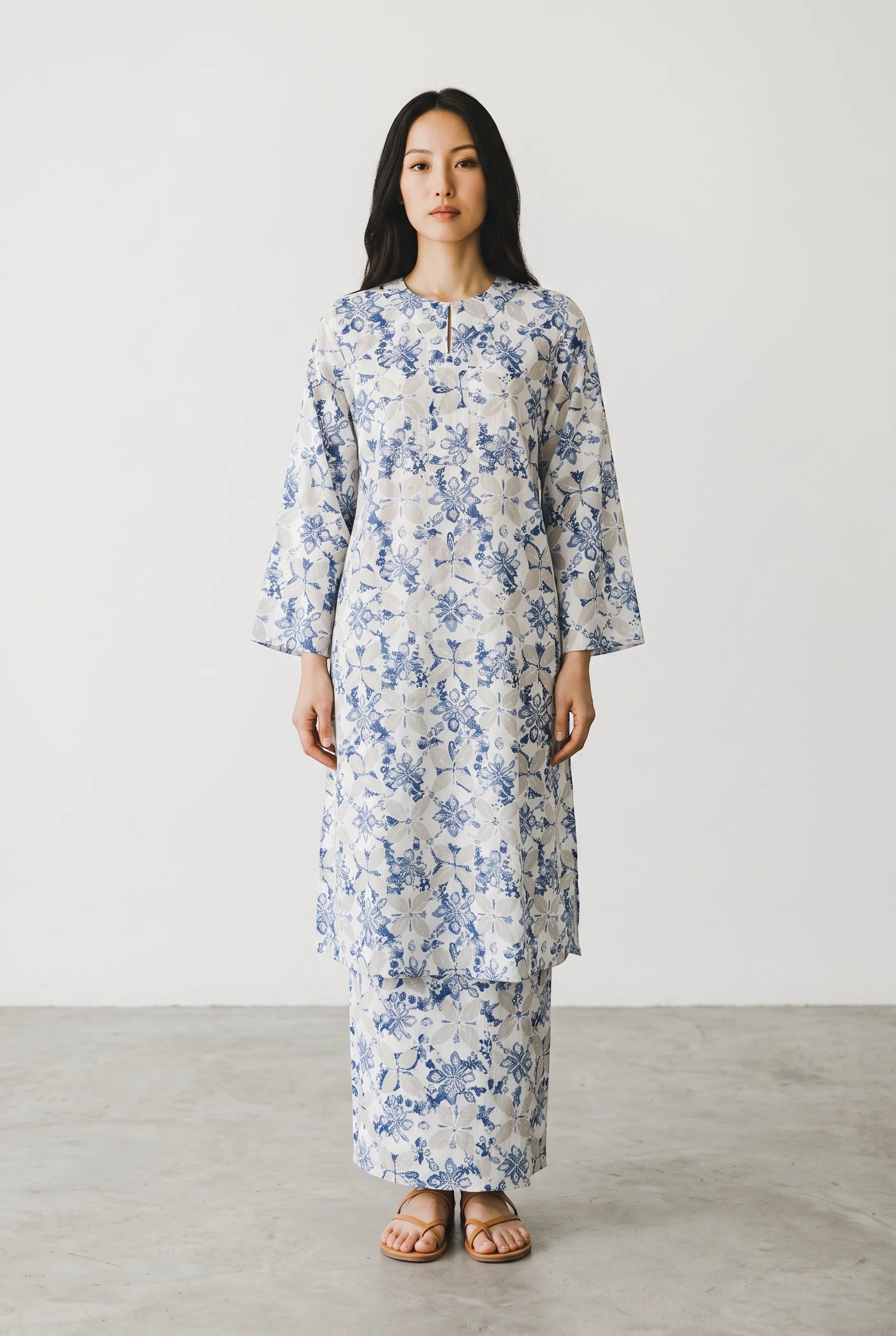 A model wearing a PARCA white midi top and matching sarung with a blue floral print, featuring long sleeves.