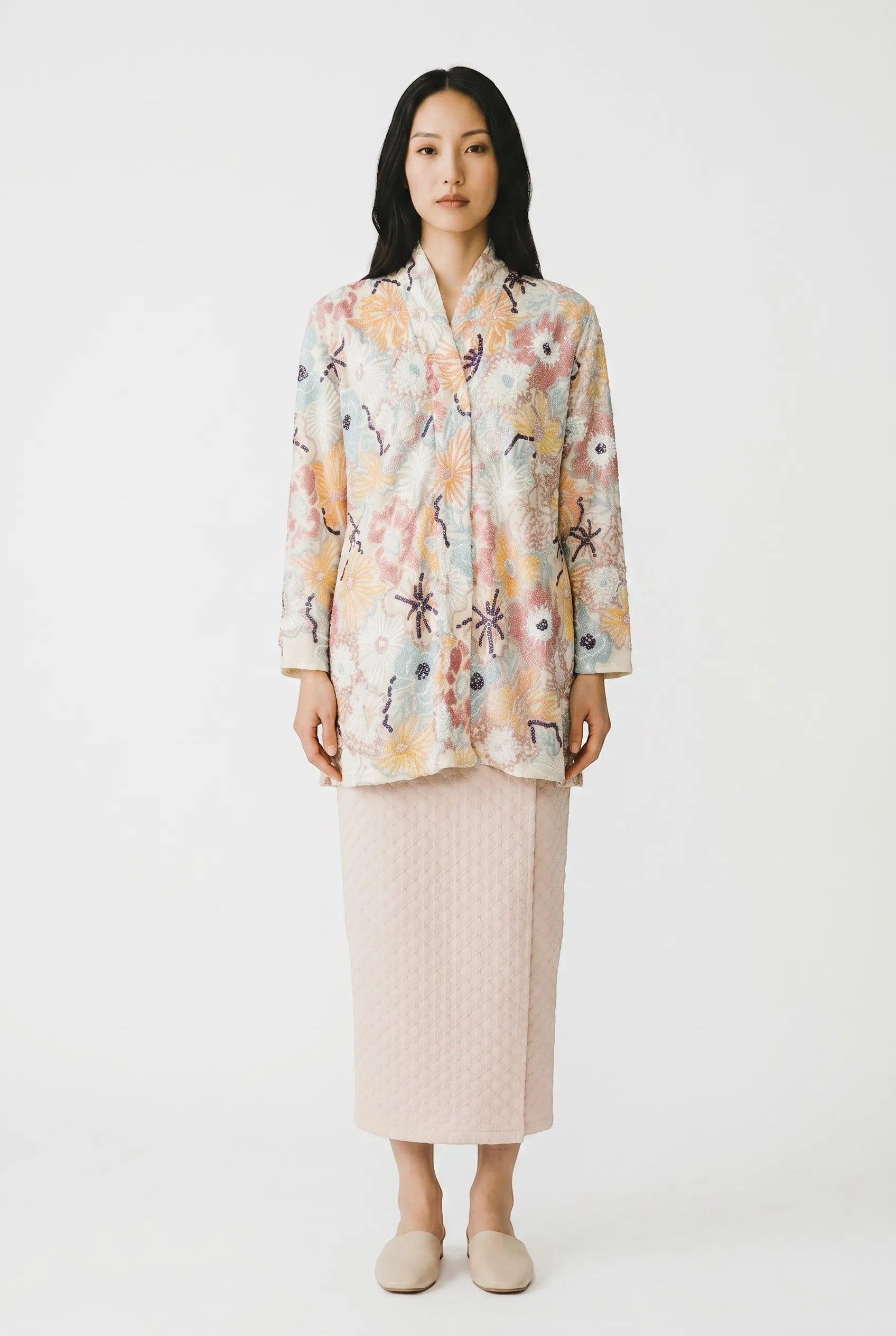 PARCA Naira Kimono kebaya in white with colourful floral embroidery and sequins. Long sleeves, V-neck. Paired with a pale pink textured wrap skirt.