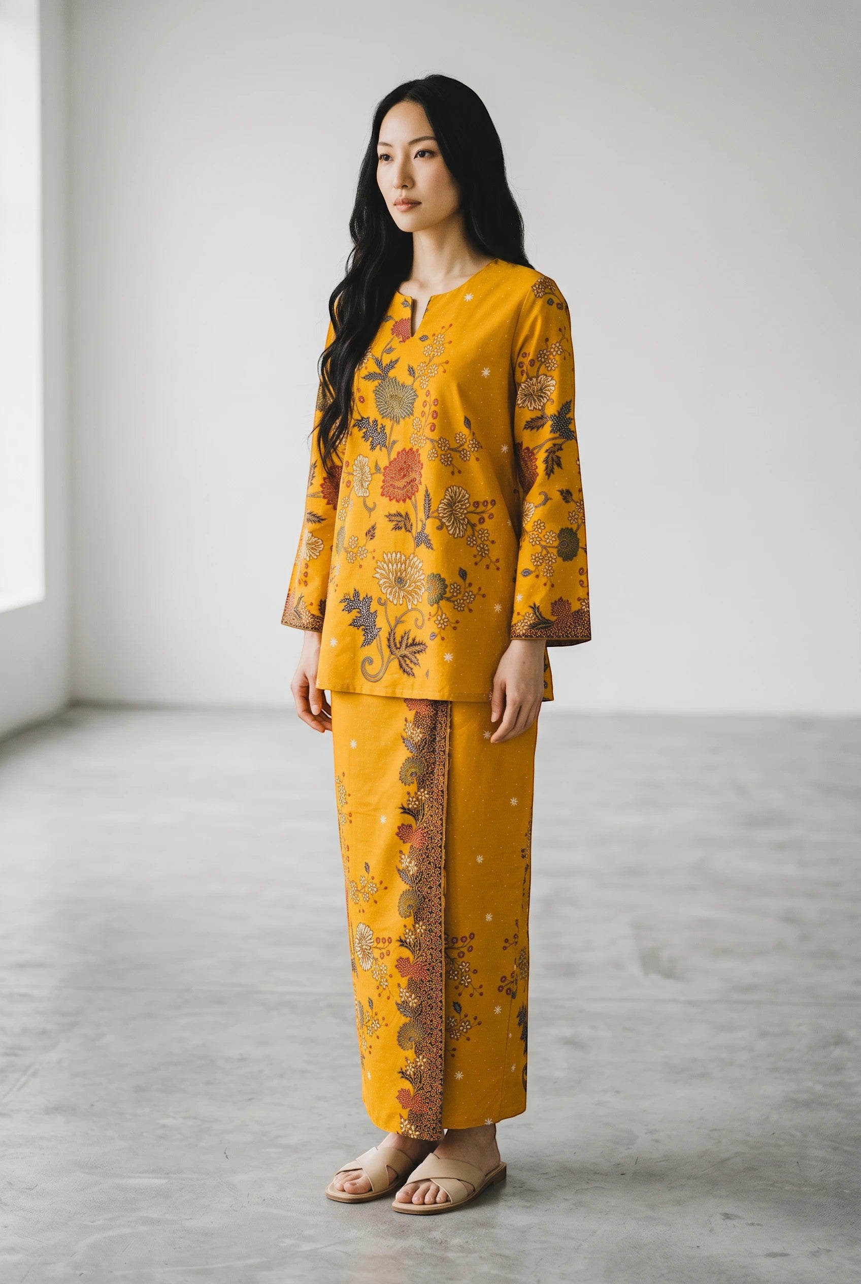 A model wearing a yellow PARCA cotton top and matching sarung with a floral batik-style print in a bright studio.