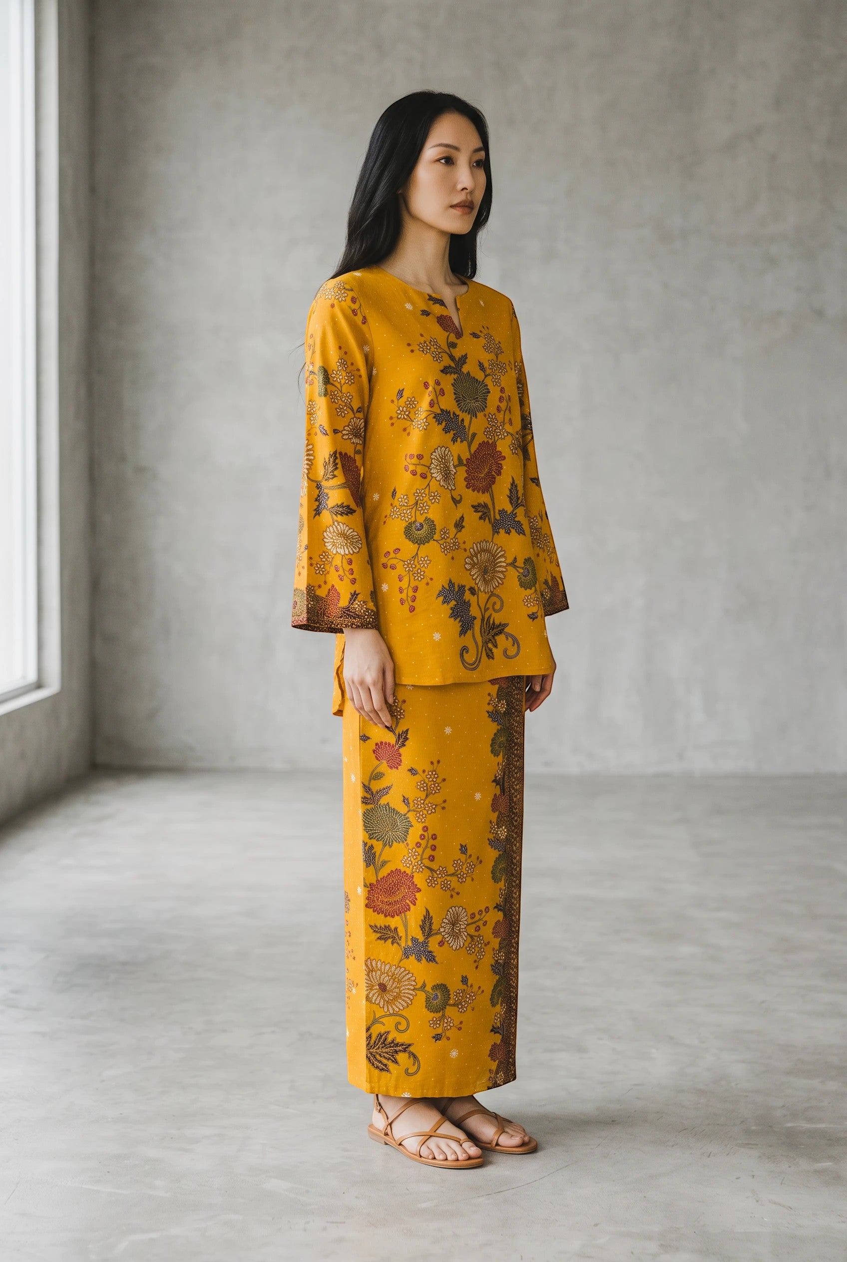 Model wearing a yellow PARCA cotton top and matching sarung with floral batik print in a minimalist studio setting