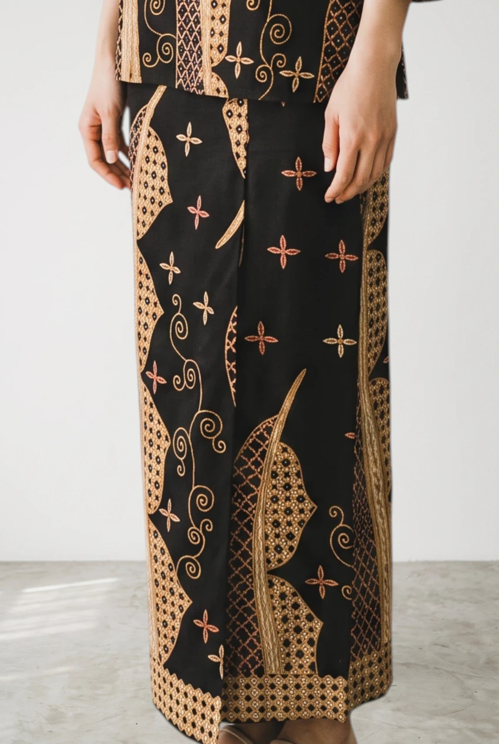 Model wearing a PARCA black cotton top and matching maxi sarung with traditional batik-inspired patterns