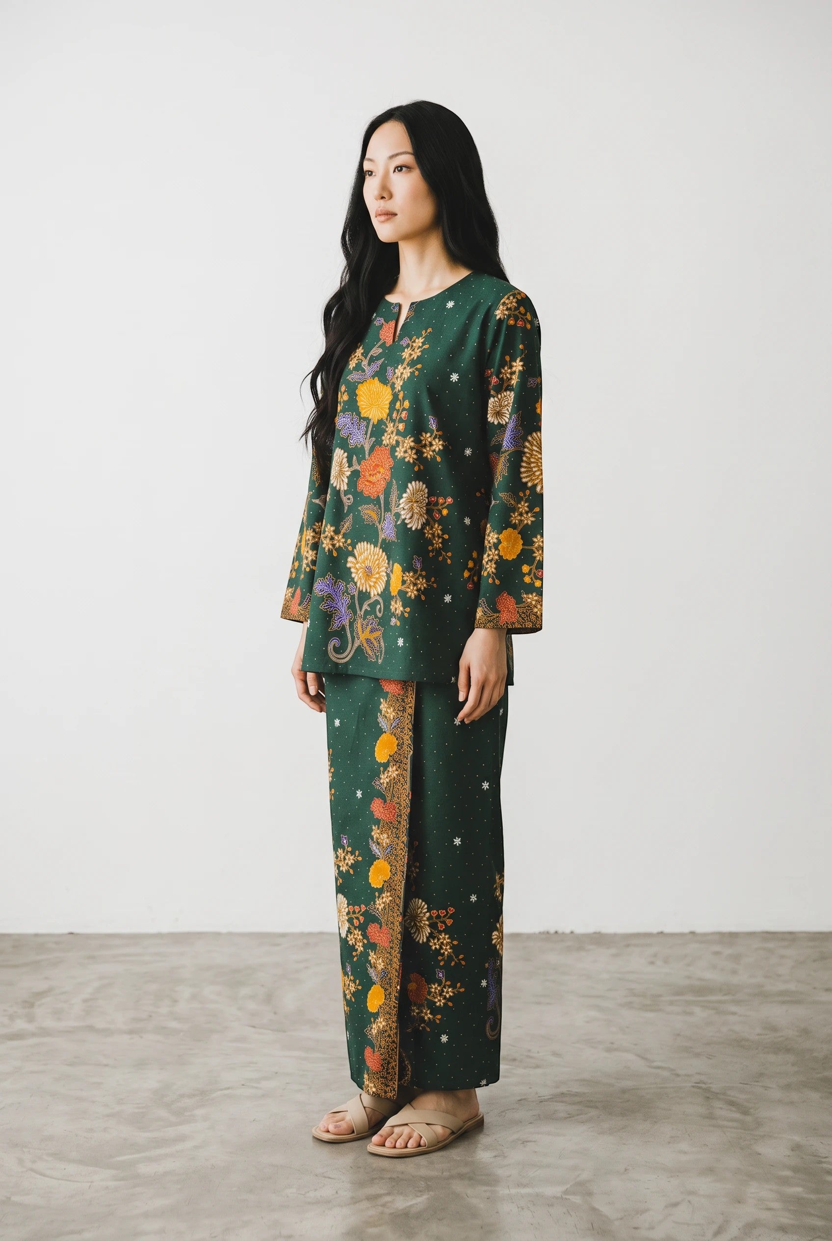 A model wearing a PARCA green cotton set featuring a floral print long-sleeve top and a matching maxi sarung skirt.