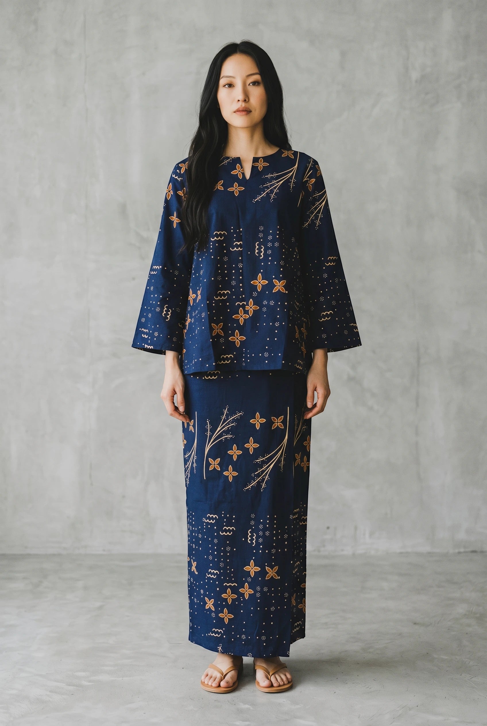 A woman wearing a PARCA Mawaddah two-piece set in navy blue with a gold floral batik-inspired print.