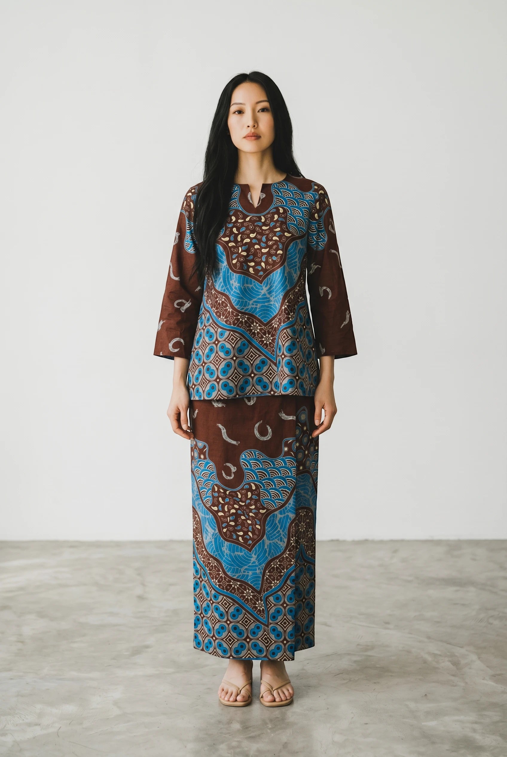 Model wearing a PARCA Mustika brown and blue batik print two-piece set with a long skirt and three-quarter sleeve top.