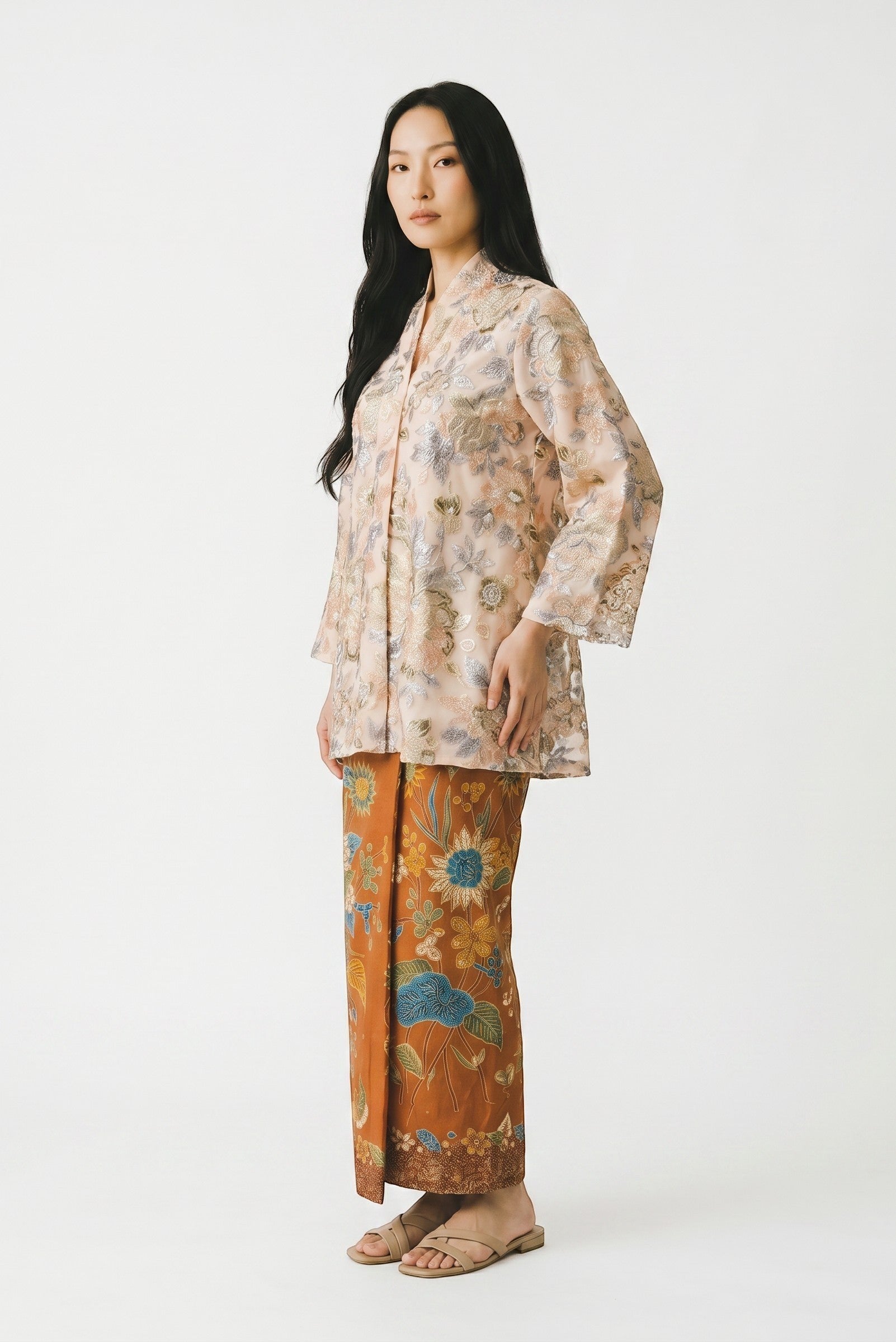 PARCA Naira Kimono kebaya in peach with intricate floral embroidery and bell sleeves, paired with a brown batik sarong.