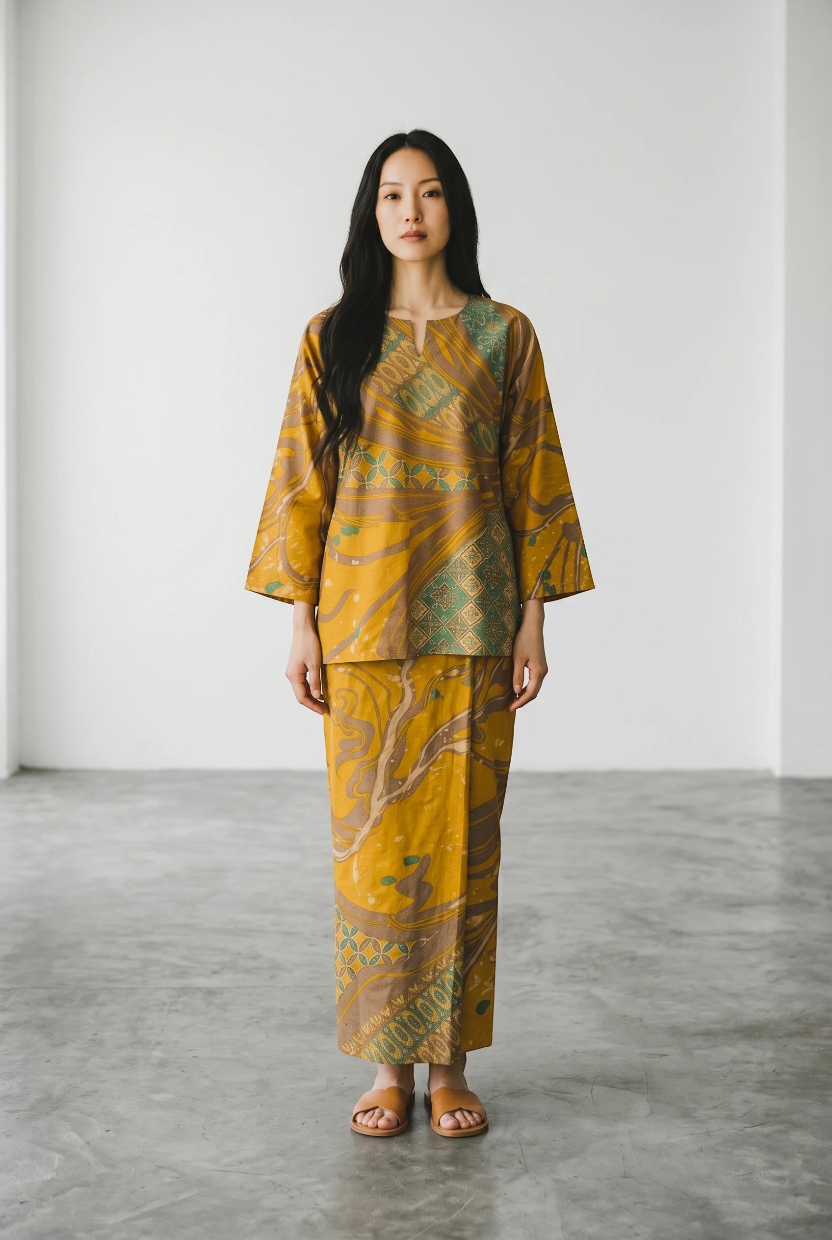 Model wearing a PARCA Natalia yellow batik print two-piece set with a long-sleeve top and matching sarong skirt.