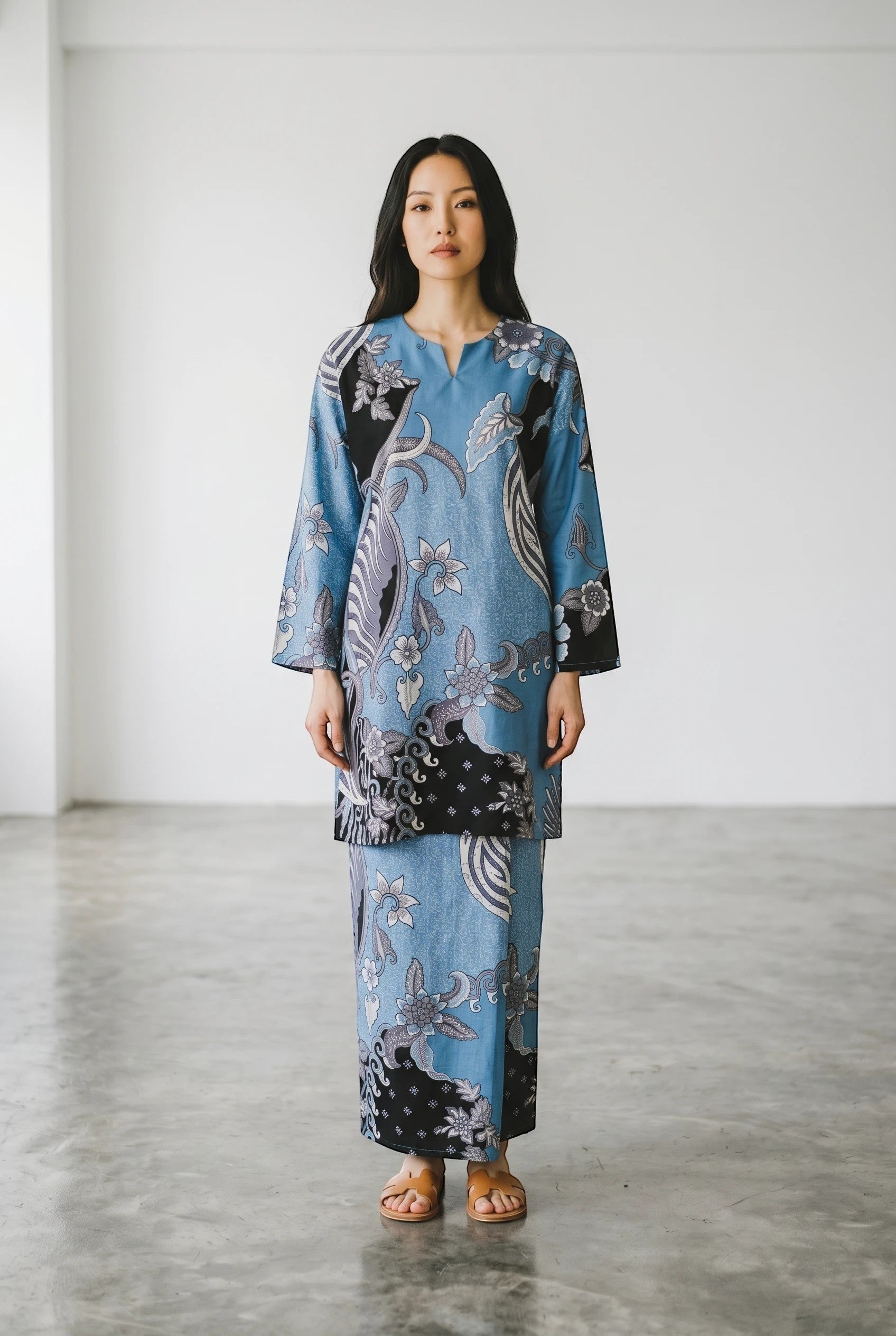 Model wearing a blue PARCA Nazima set with a long-sleeved top and matching maxi sarung featuring a floral batik print.